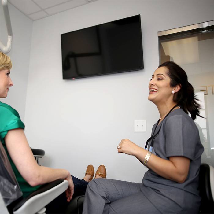 Dentist and patient in exam room with TV on wall above dental chair