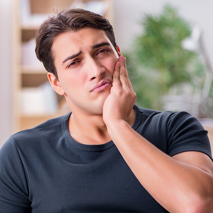 Man in need of emergency dentistry holding cheek in pain