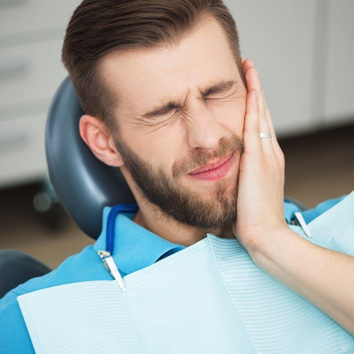 Man in dental chair holding jaw in pain before tooth extraction