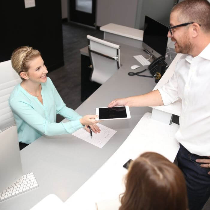 Smiling man handing tablet to dental office team member in Frisco