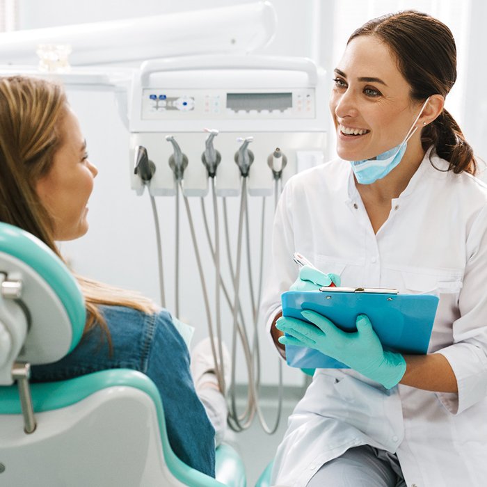 Dentist smiling at patient while talking to patient and taking notes