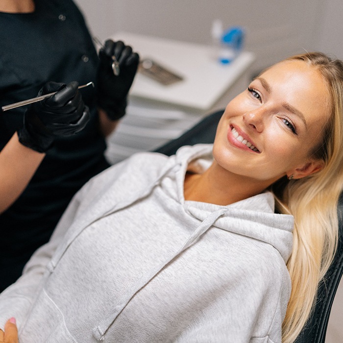 Woman in grey sweatshirt smiling while sitting in treatment chair
