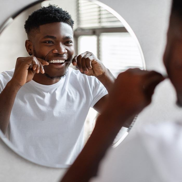 Man in white shirt smiling at reflection while flossing