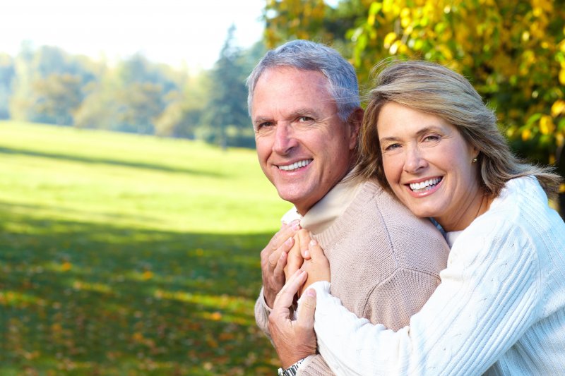 Older couple smiling and hugging after visiting a cosmetic dentist.