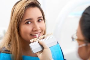 dentist holding veneers up to a young woman’s smile 